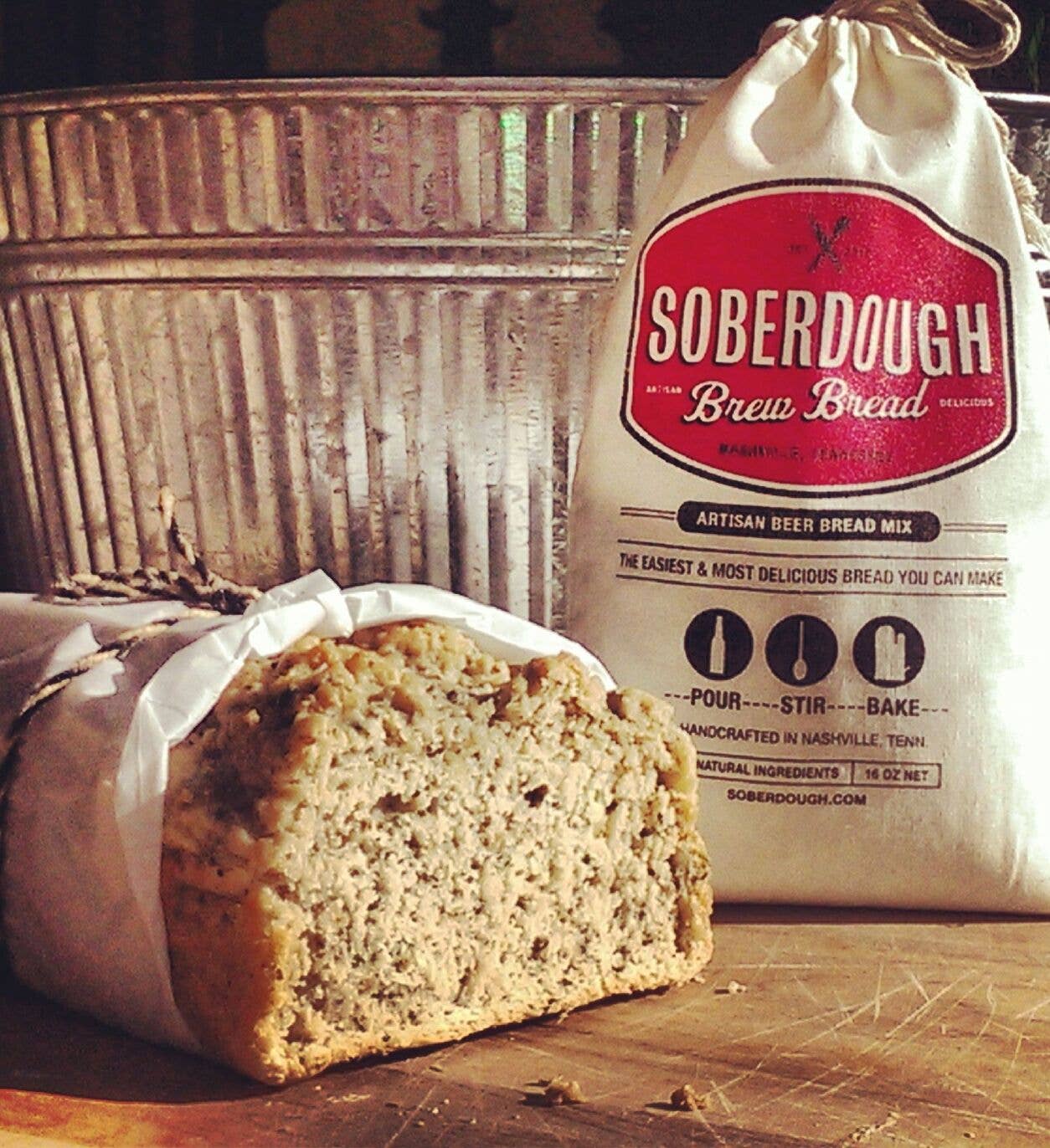 Loaf of bread with a bag of Soberdough Brew Bread mix on a wooden surface.