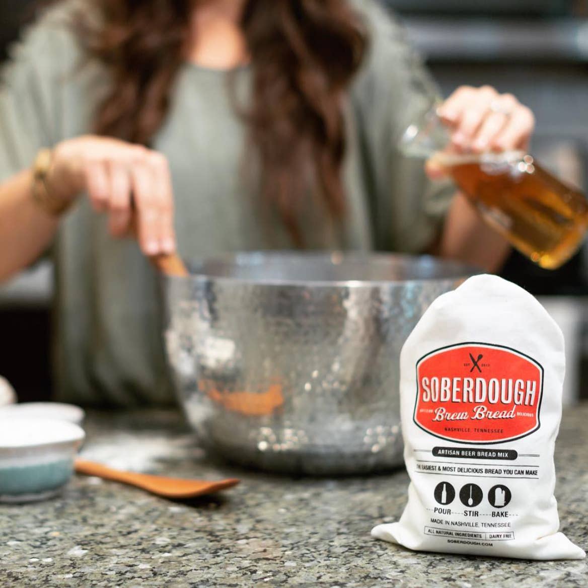 Person preparing a meal with a bag of Soberdough Brew Bread mix on a countertop.