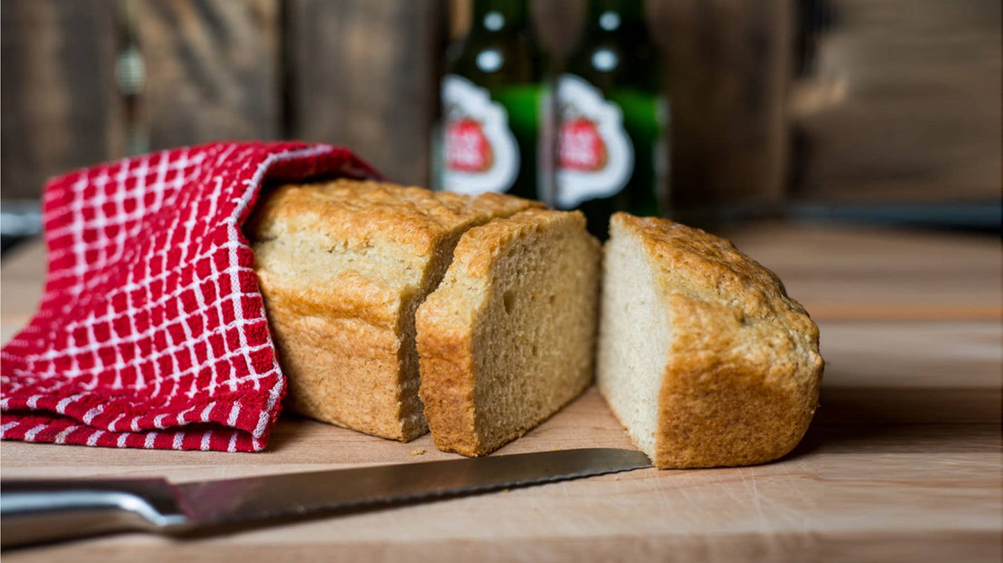 Loaf of bread with a knife on a wooden surface, with two bottles in the background.