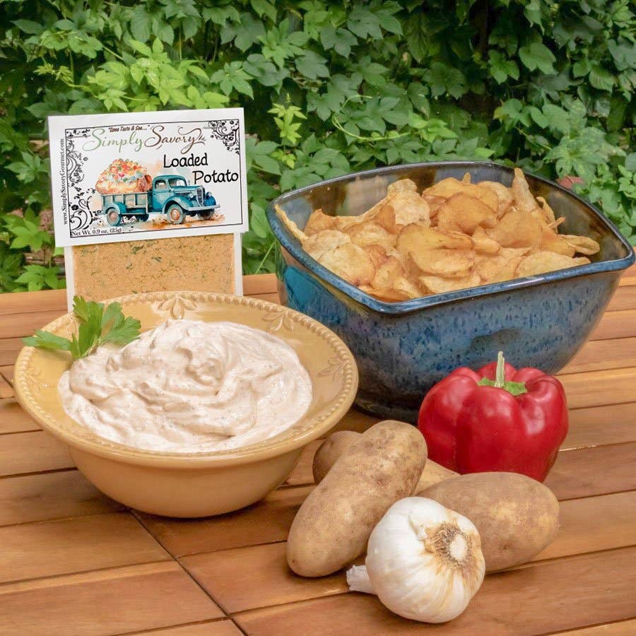Dip with potatoes, garlic, and a pepper on a wooden surface with a 'Simply Sauzy' sign in the background.