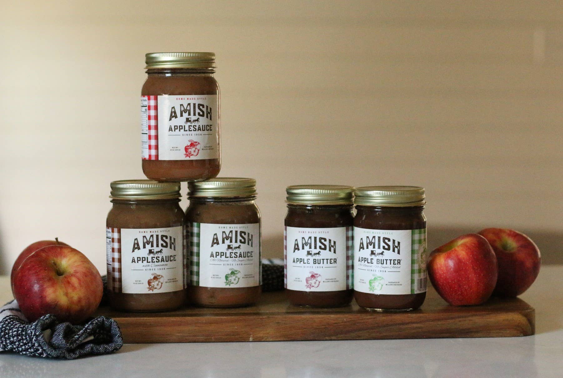 Jars of Amish Applesauce and Apple Butter on a wooden board with apples.